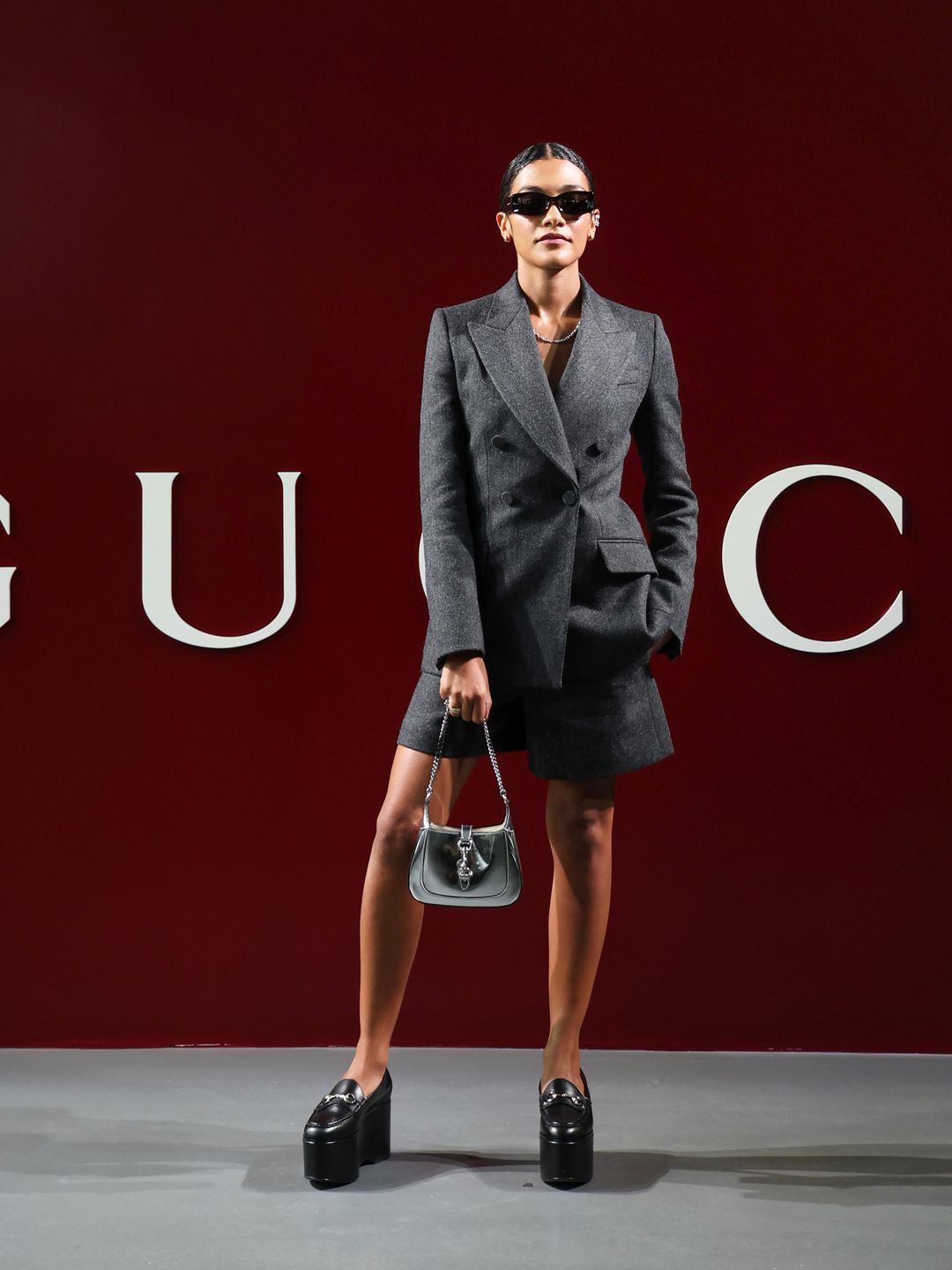 Olivia Dean attends the Gucci Women's Fall Winter 2024 Fashion Show in a grey blazer and shorts combo, topping off the look with a pair of platform loafers.