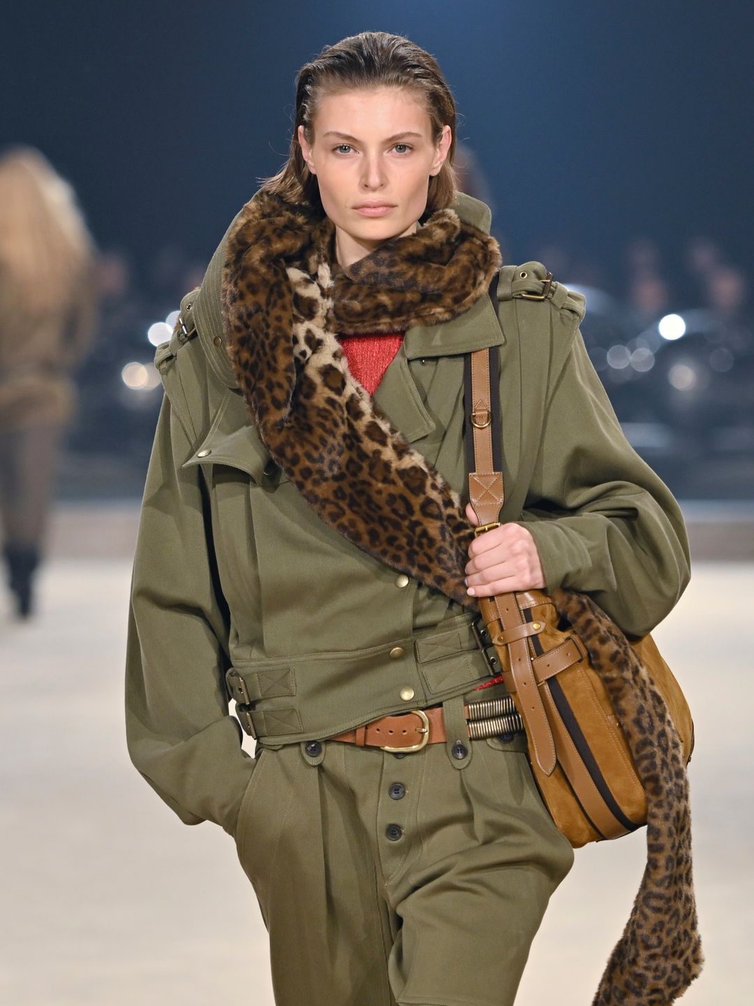 A model walks the runway during the Isabel Marant Ready to Wear Fall/Winter 2024-2025 fashion show in a matching green jacket and torusers combo with a fluffy cheetah print scarf