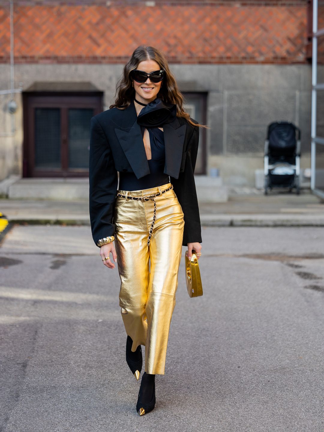 Woman wearing gold pants, Coperni bag, black cropped blazer, top, sunglasses, ankle boots 
