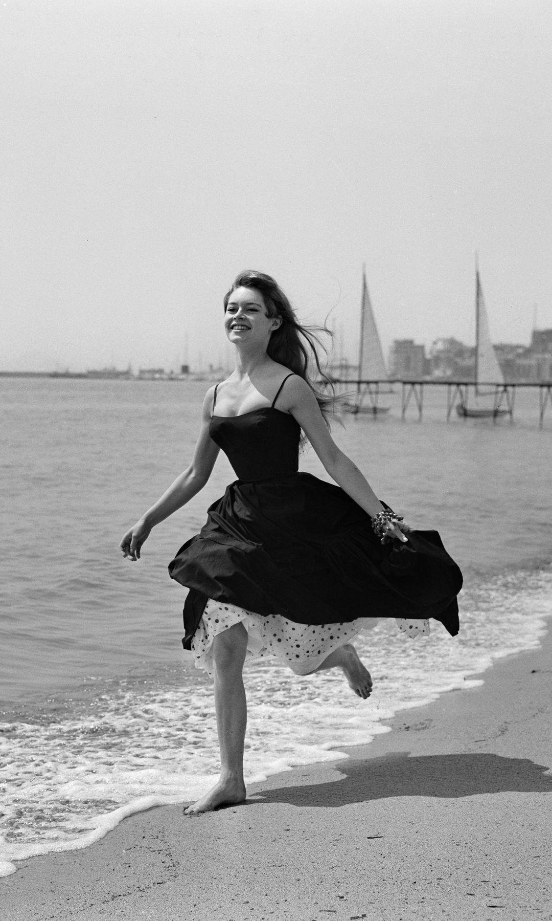 Brigitte Bardot runs barefoot along the beach in a black dress