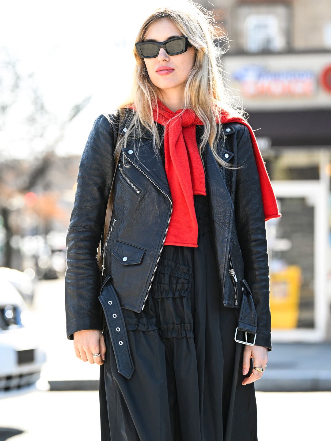 Aemilia Fay dons a black biker jacket over a black dress with ruffle accents, complete with a pop of colour in the form of an over the shoulder red jumper.