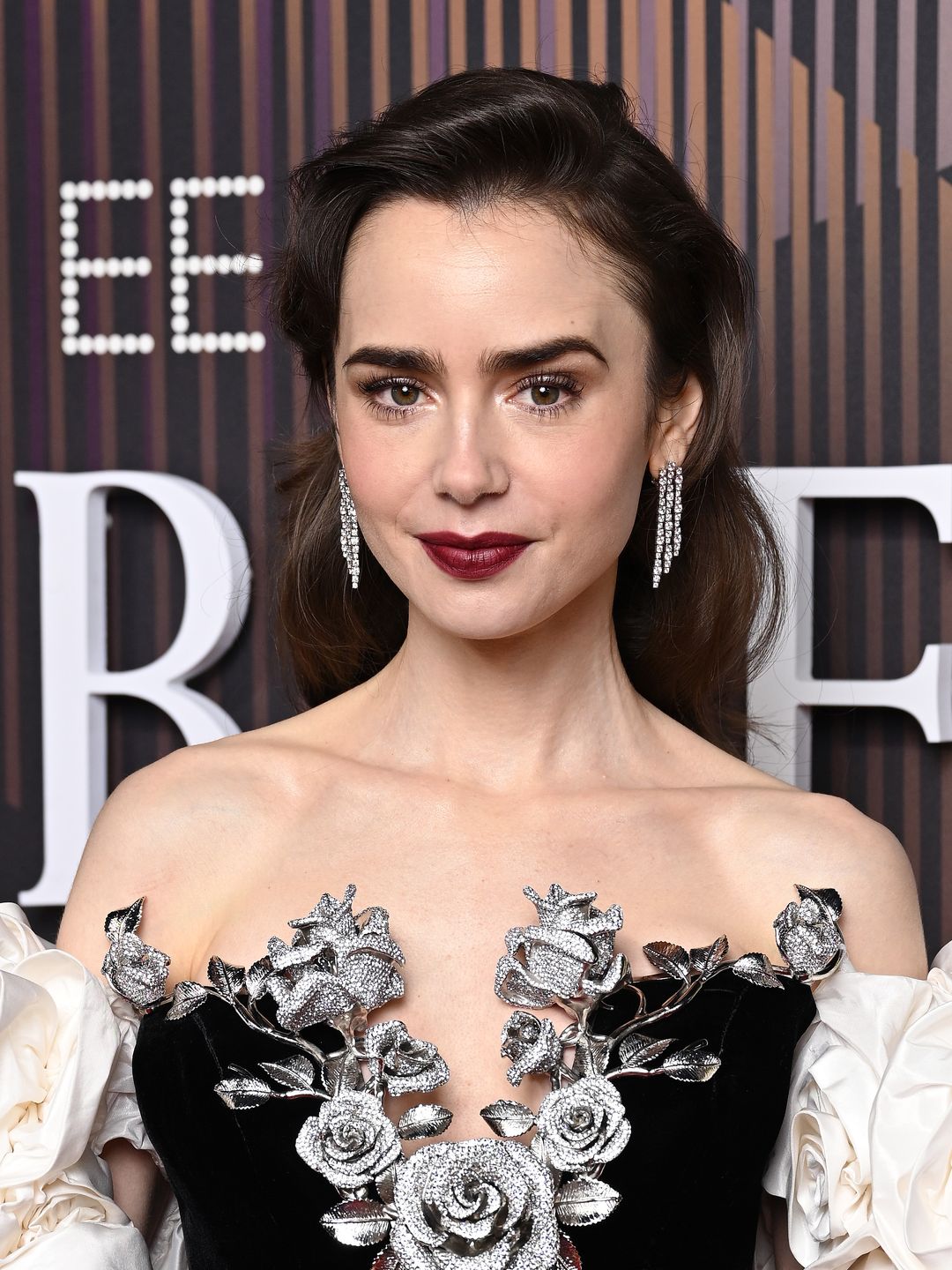 Lily Collins wearing a monochrome gown with 3D roses and a wine-hued lip at the BAFTAs