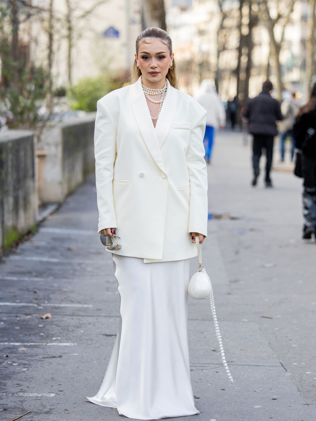 Influencer is wearing a long white dress with a white blazer and pearlescent bag