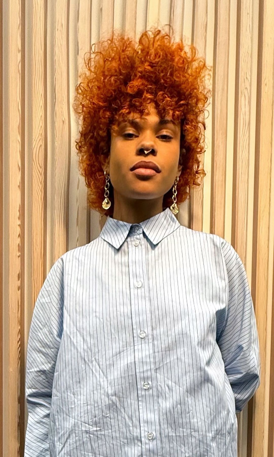 A woman in a striped shirt looks to the camera. Her hair is a vibrant shade of pale orange