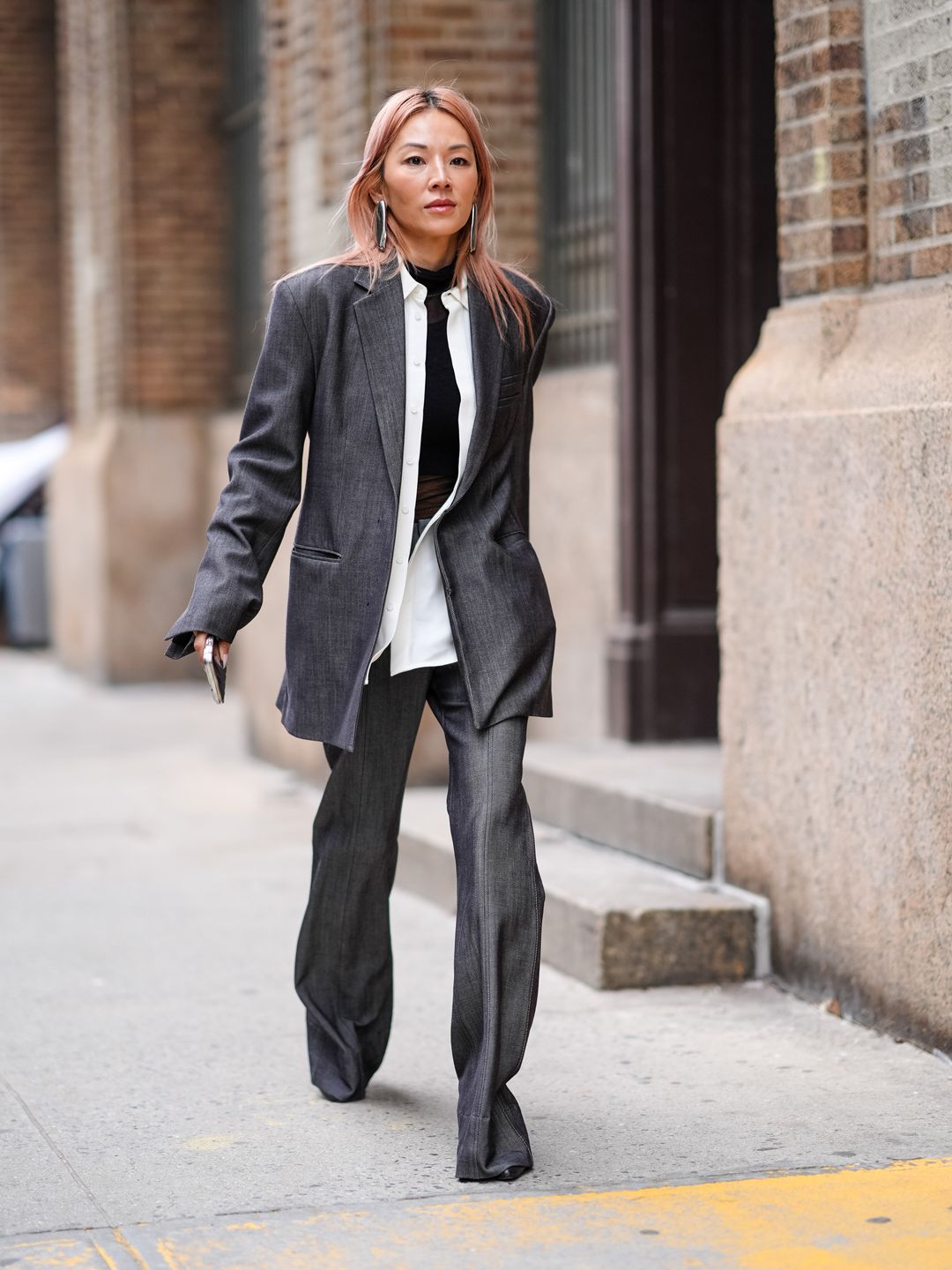 Tina Leung wears earrings, a black turtleneck top, a white shirt, a gray oversized blazer jacket , flared pants, outside Proenza Schouler in NYC