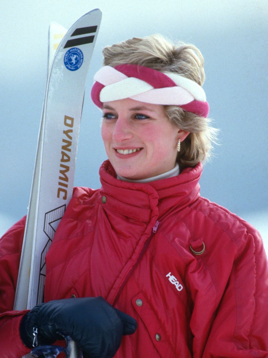 Princess Diana sporting a classic red ski suit and a braided headband. 