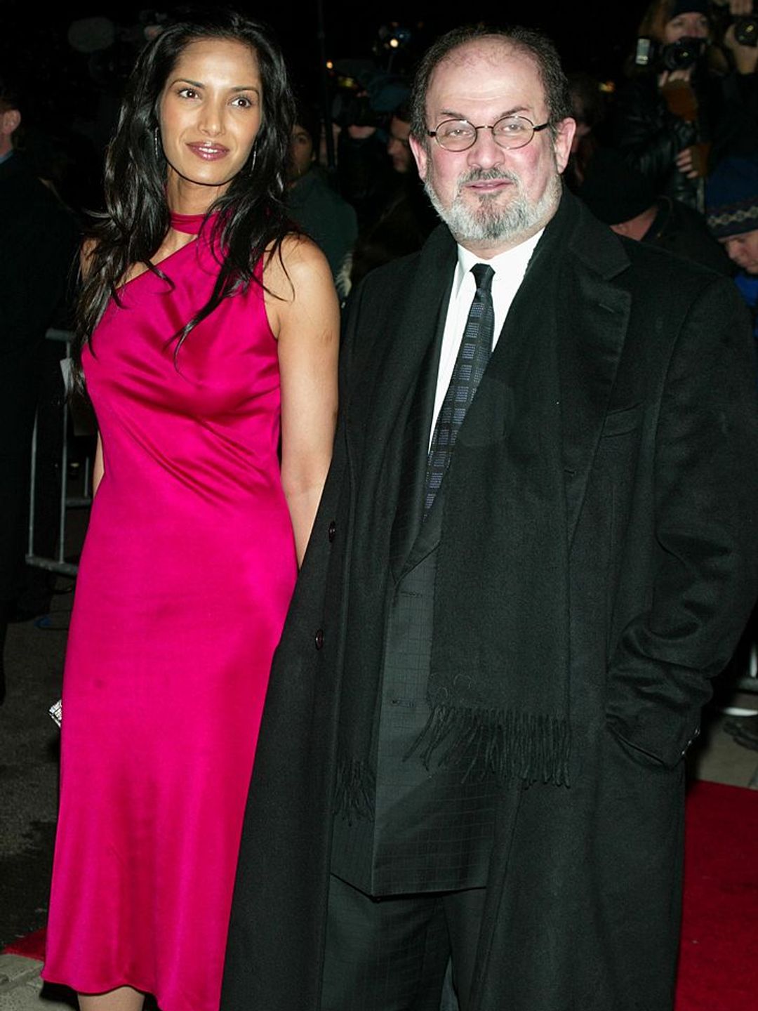 Padma Lakshmi wearing a pink satin dress as she holds hands with Salman Rushdie. 