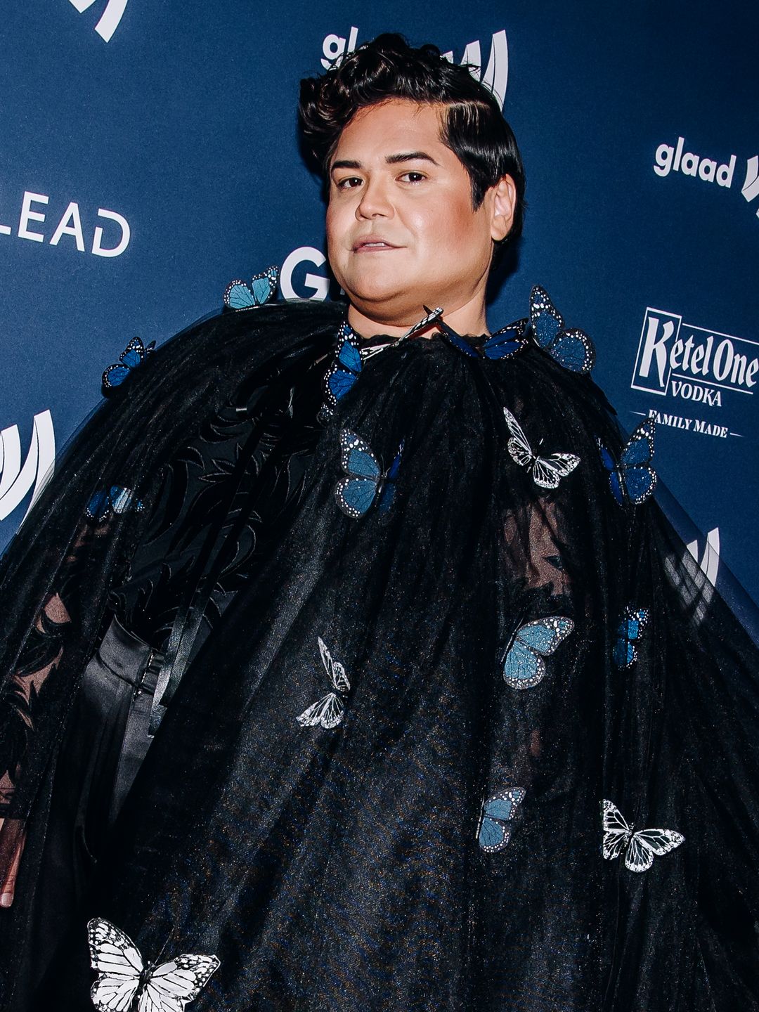 Harvey Guillen at the GLAAD Awards in a butterfly strewn black cape