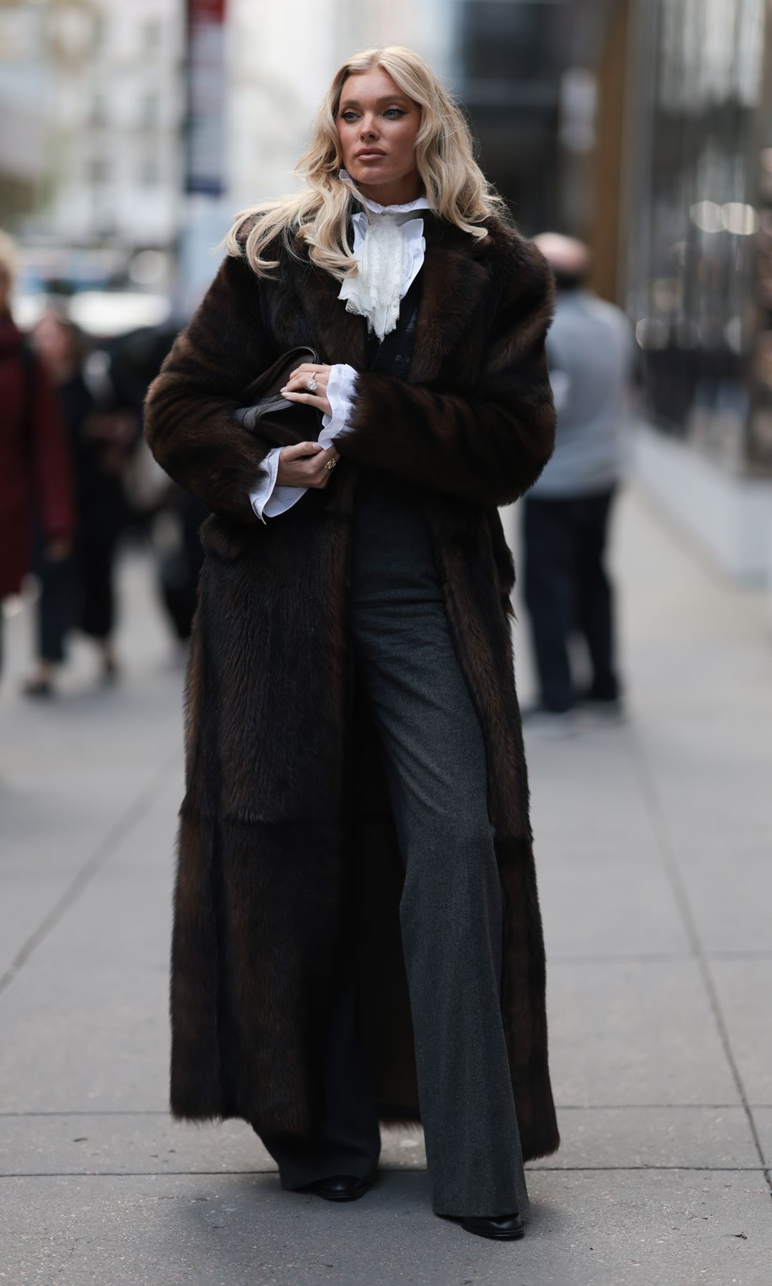Elsa Hosk seen wearing dark brown full-length fur coat draped over a romantic white ruffled blouse, tailored charcoal grey waistcoat, dark grey wide-leg suit trousers, Ralph Lauren black leather clutch bag and black leather pointed boots, outside the Ralph Lauren Show, during New York Fashion Week, on September 10, 2025 in New York City