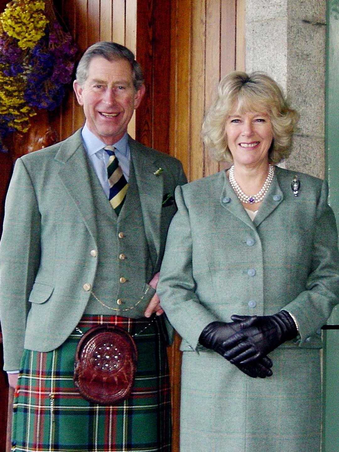 King Charles in a kilt standing with Queen Camilla in a green outfit