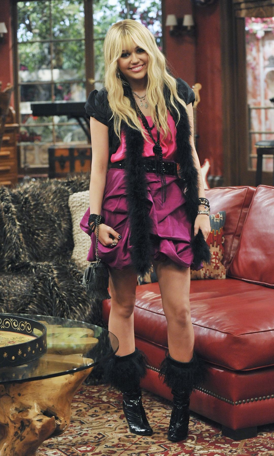 Miley Cyrus as Hannah Montana posing infront of a red couch in a pink outfit