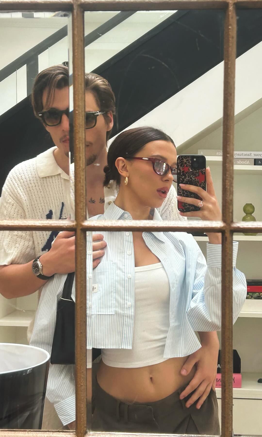 Millie Bobby Brown poses for a mirror selfie at home with her husband Jake in a stripe crop shirt and ribbed tank top