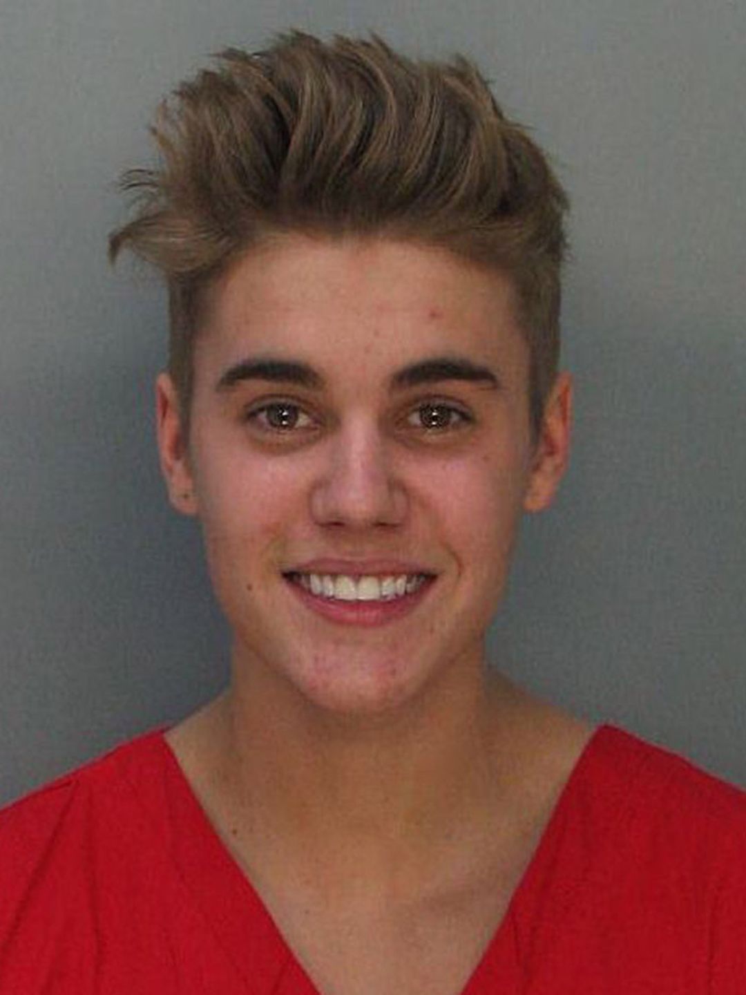 Justin Bieber smiling for mugshot in orange outfit