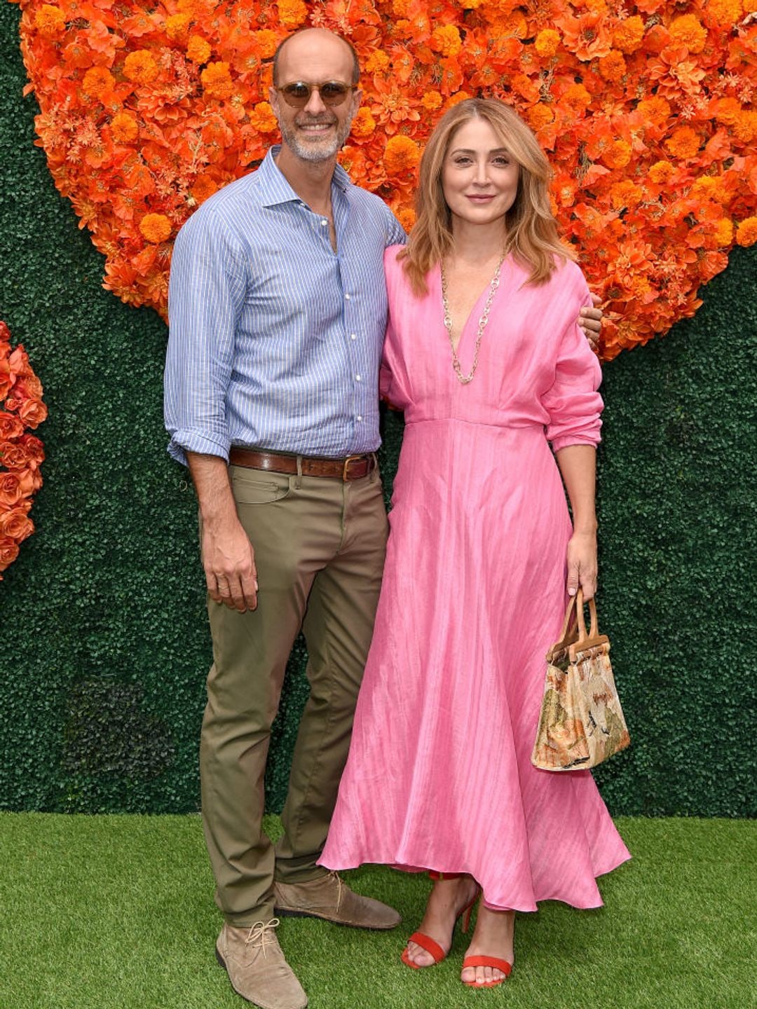 Sasha Alexander cuddled up with Edoardo Ponti at a press event. She is wearing a pink midi dress, while he is wearing a blue striped shirt and chinos. 