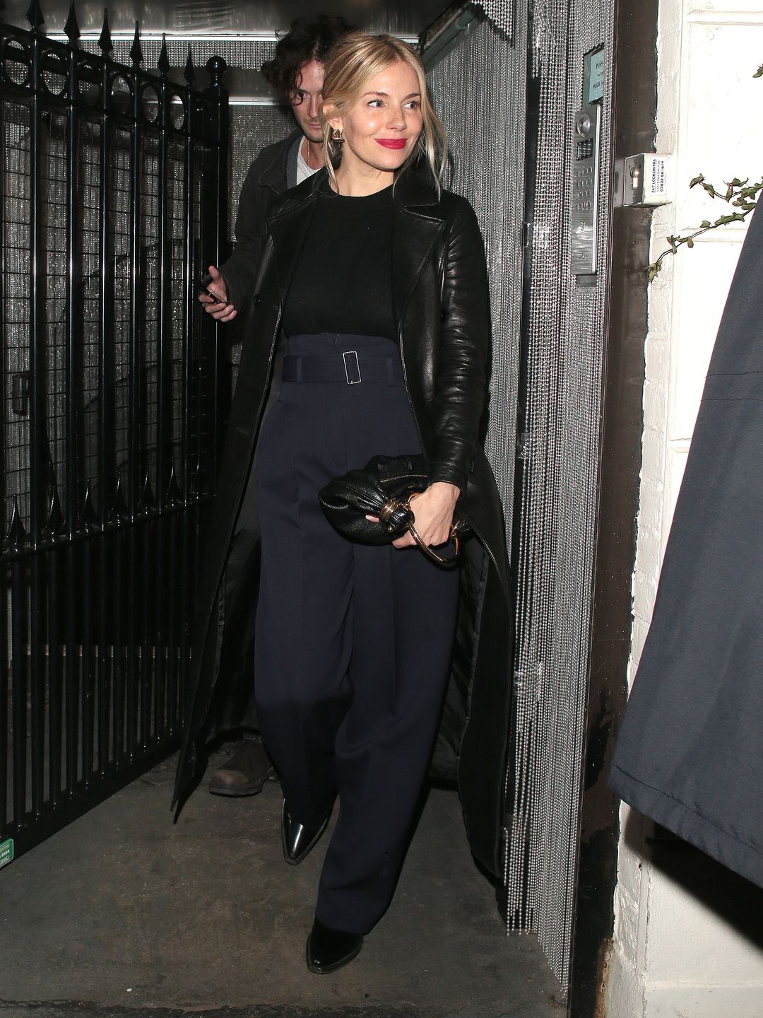 Sienna Miller wearing navy trousers and a black trench 