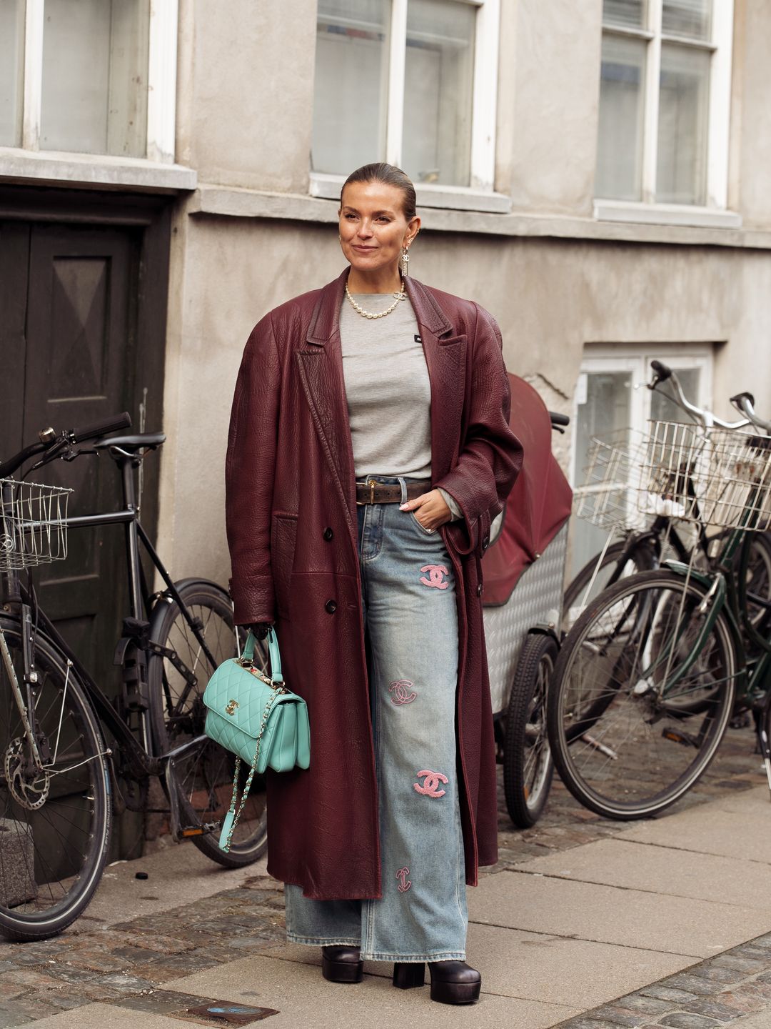 COPENHAGEN, DENMARK - JANUARY 29: Janka Polliani is wearing Chanel blue jeans with a pink embroidered logo, a long leather burgundy coat, a grey top, and a mint green Chanel bag during the Copenhagen Fashion Week AW24 on January 29, 2024 in Copenhagen, Denmark. (Photo by Raimonda Kulikauskiene/Getty Images)