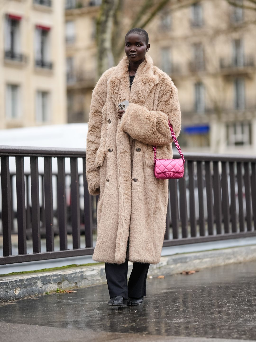  model wears a brown / beige fluffy faux fur long winter coat, black pants, neon pink quilted Chanel bag, outside Chanel, during the Haute Couture Spring/Summer 2024 