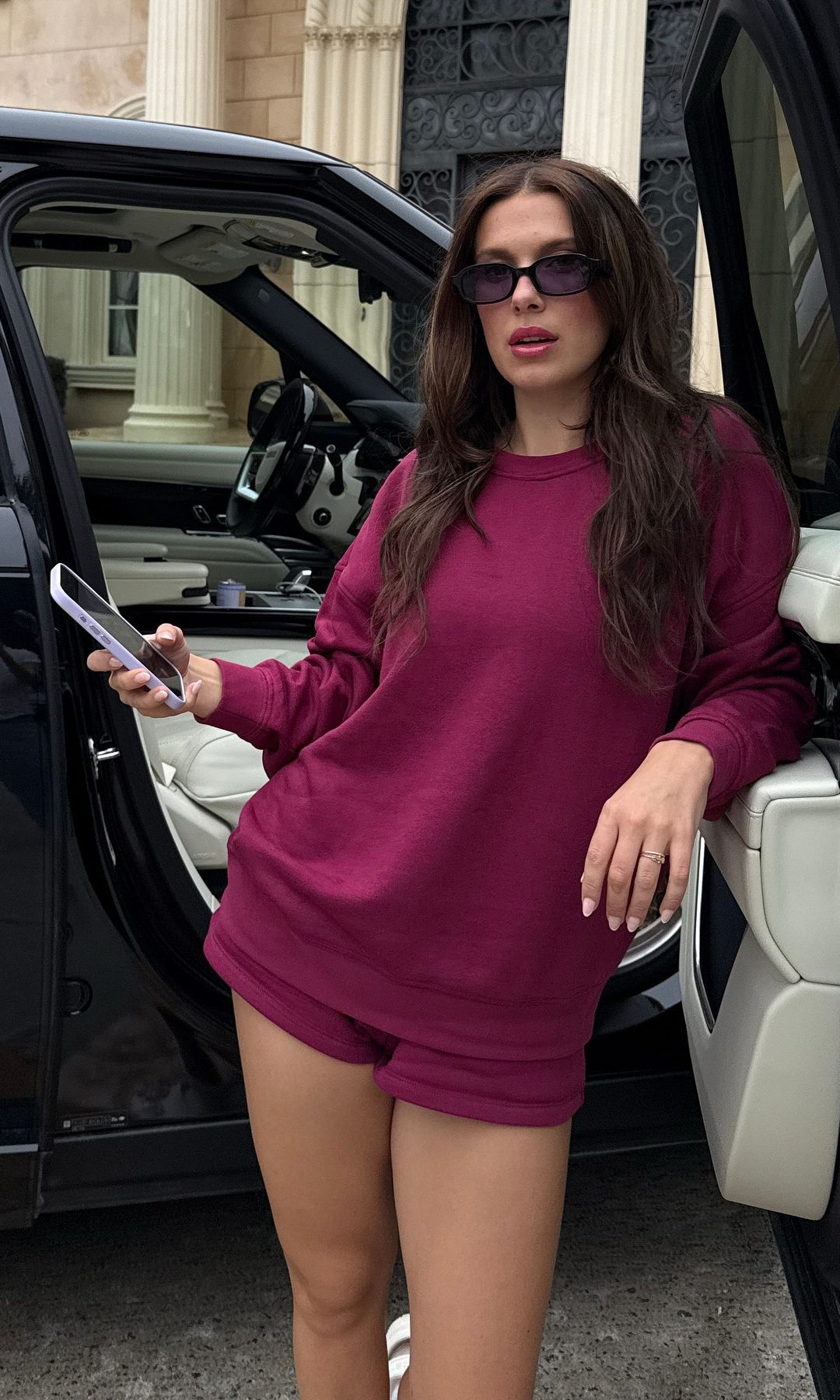 Millie Bobby Brown poses for a photo next to her car, wearing a cherry red co-ord