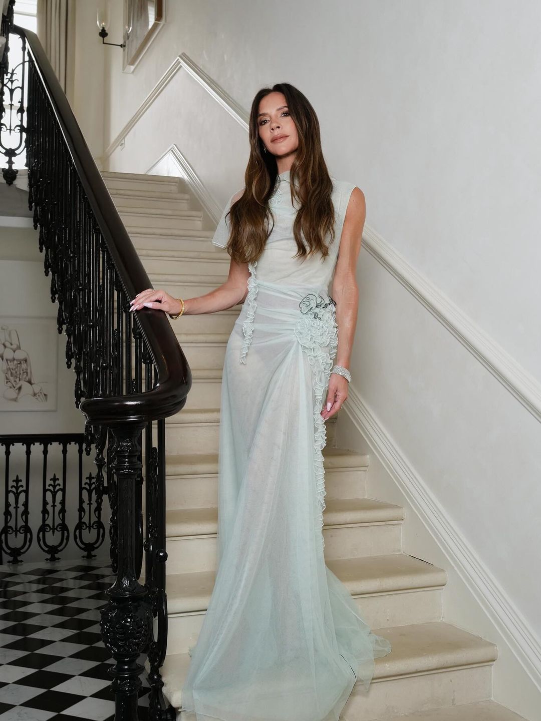 Victoria Beckham poses in a mint green sheer dress on a staircase