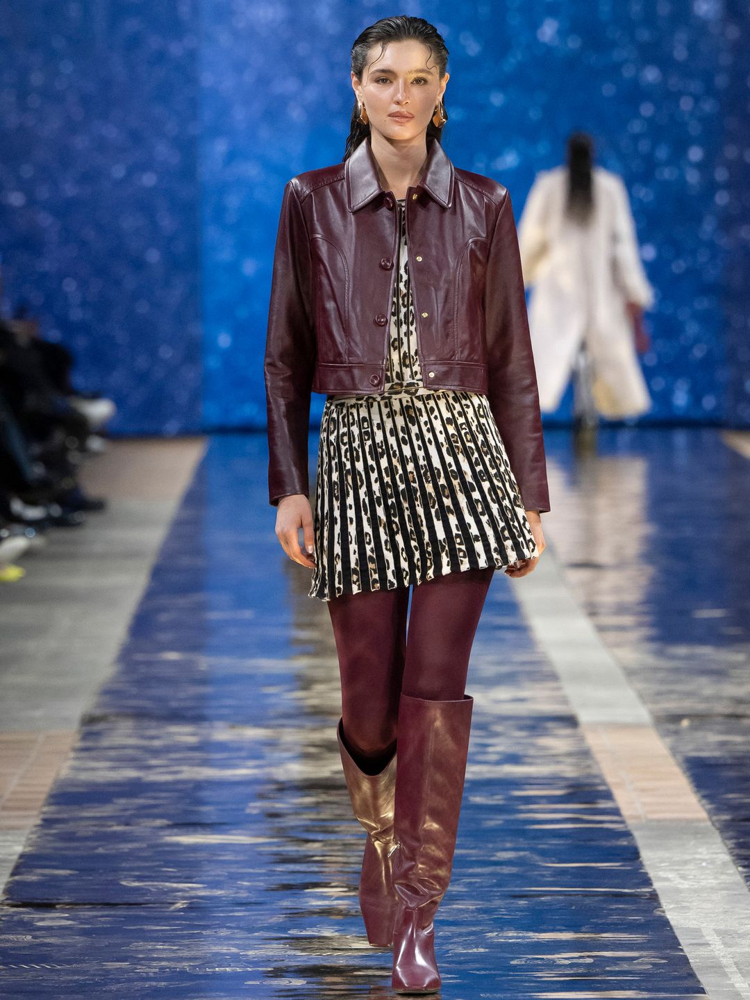 A model walks down the Marc Cain runway in a leopard print pleated dress, a burgundy leather jacket with matching tights and knee high cowboy boots. 