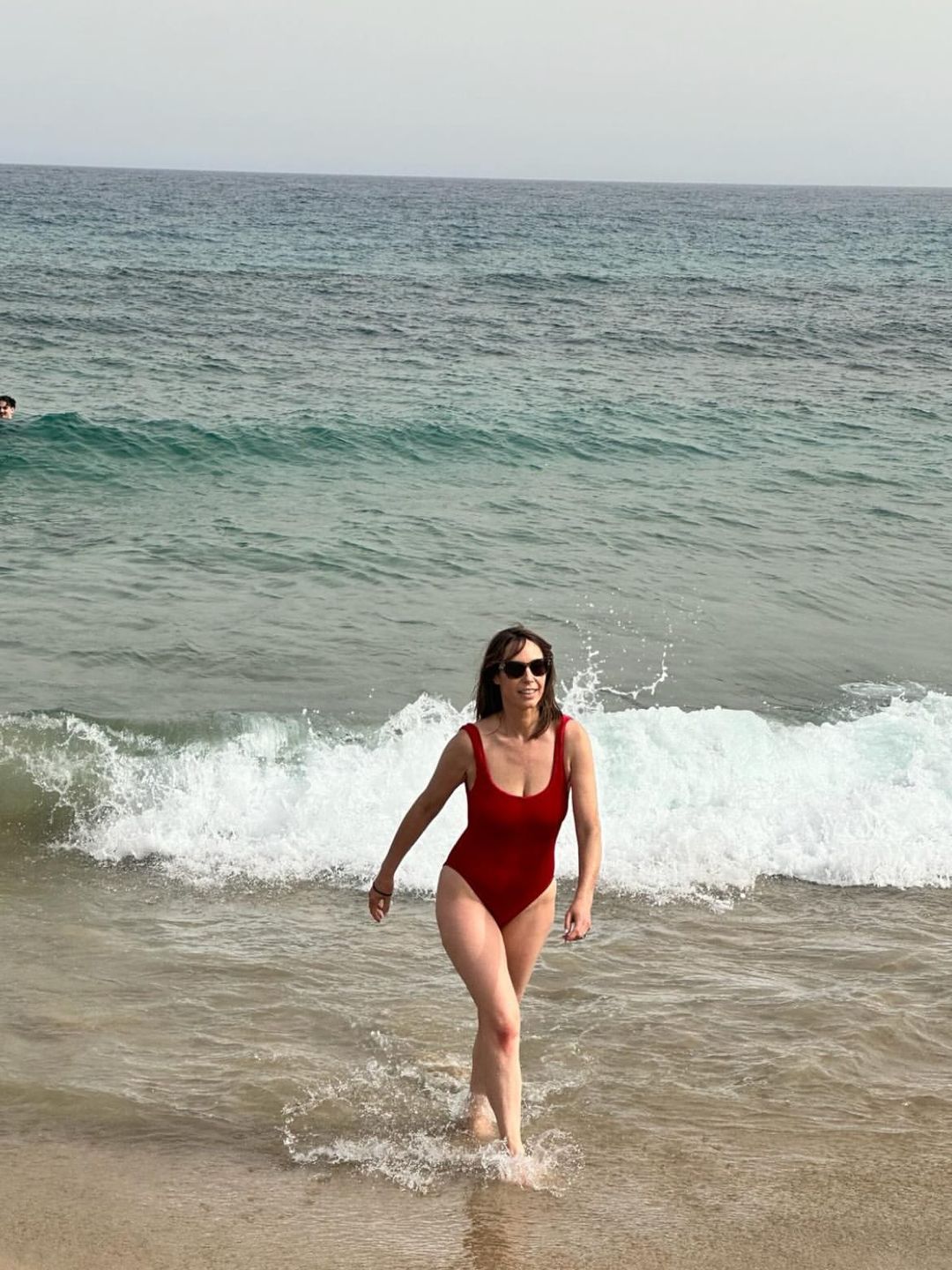 Alex Jones walking out of the ocean in a red swimsuit