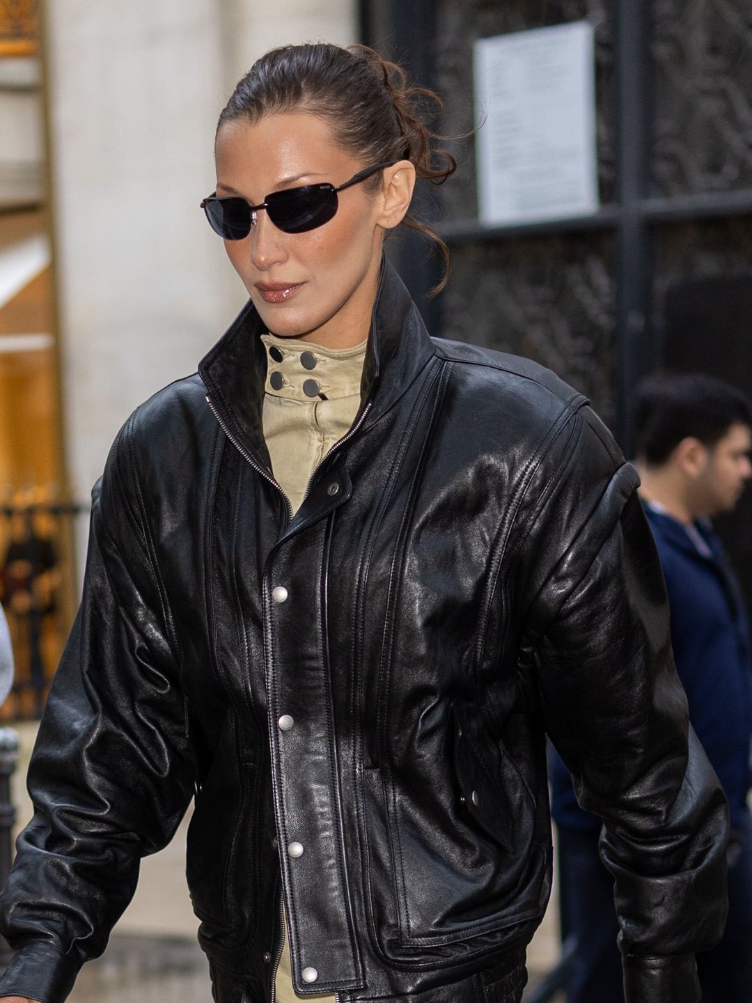 Bella Hadid is seen on September 23, 2024 in Paris, France wearing a set of black sunglasses, a leather jacket and beige dress