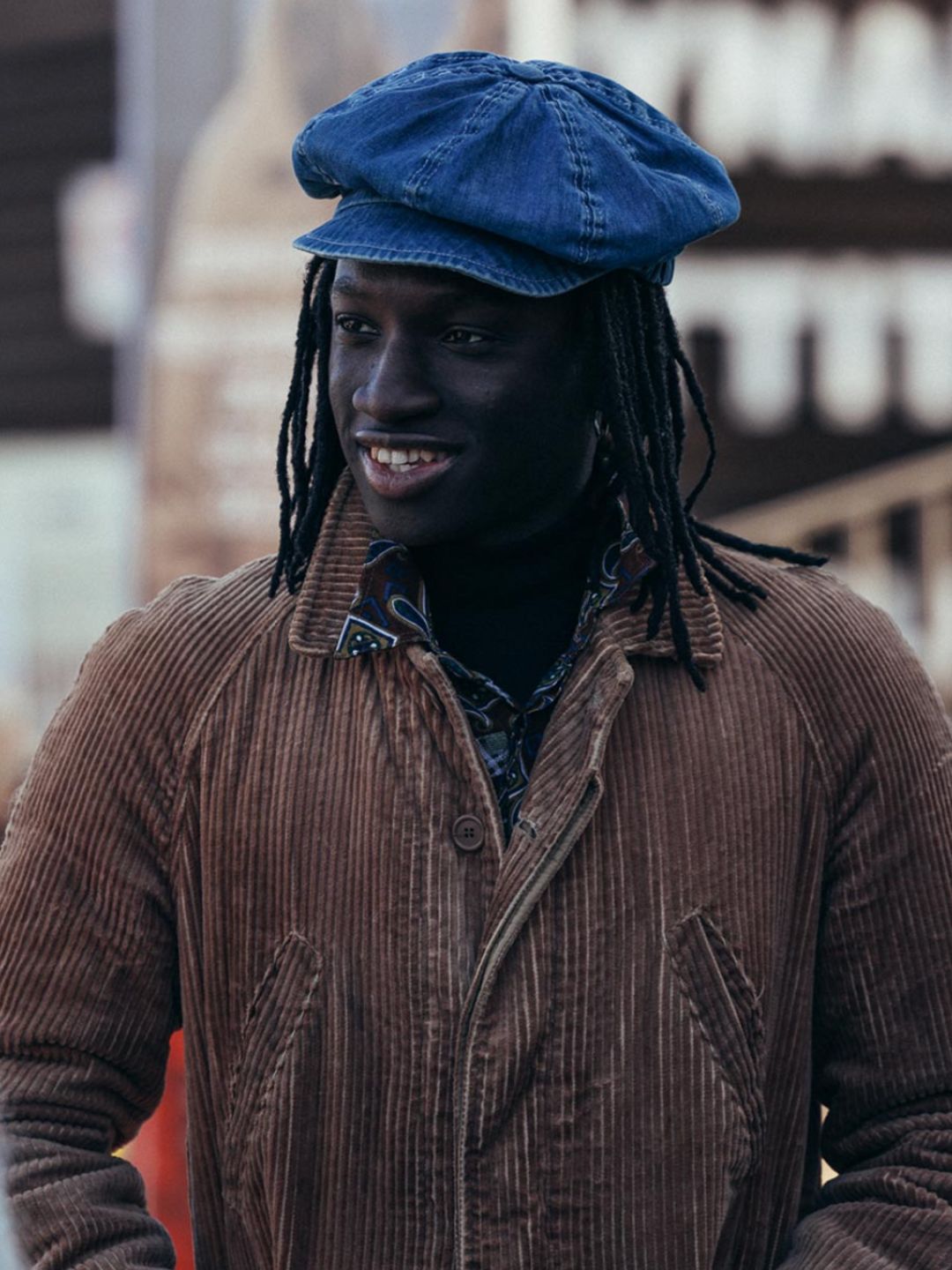 A Pitti Uomo attendee wears a denim baker boy cap and a brown corduroy jacket 