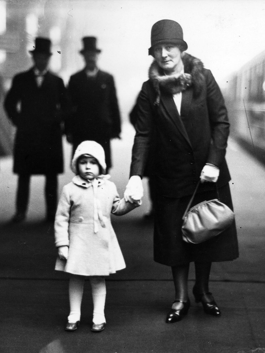 A young Queen Elizabeth holding the hand of a woman at a train station