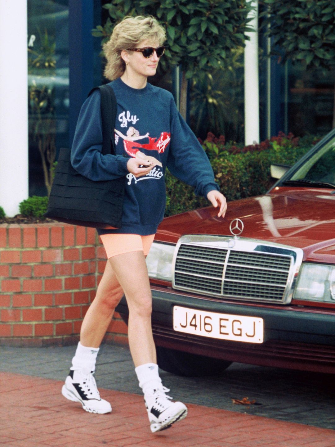 Princess Diana, Princess of Wales styles a navy Virgin Atlantic sweatshirt alongside orange cycling shorts 