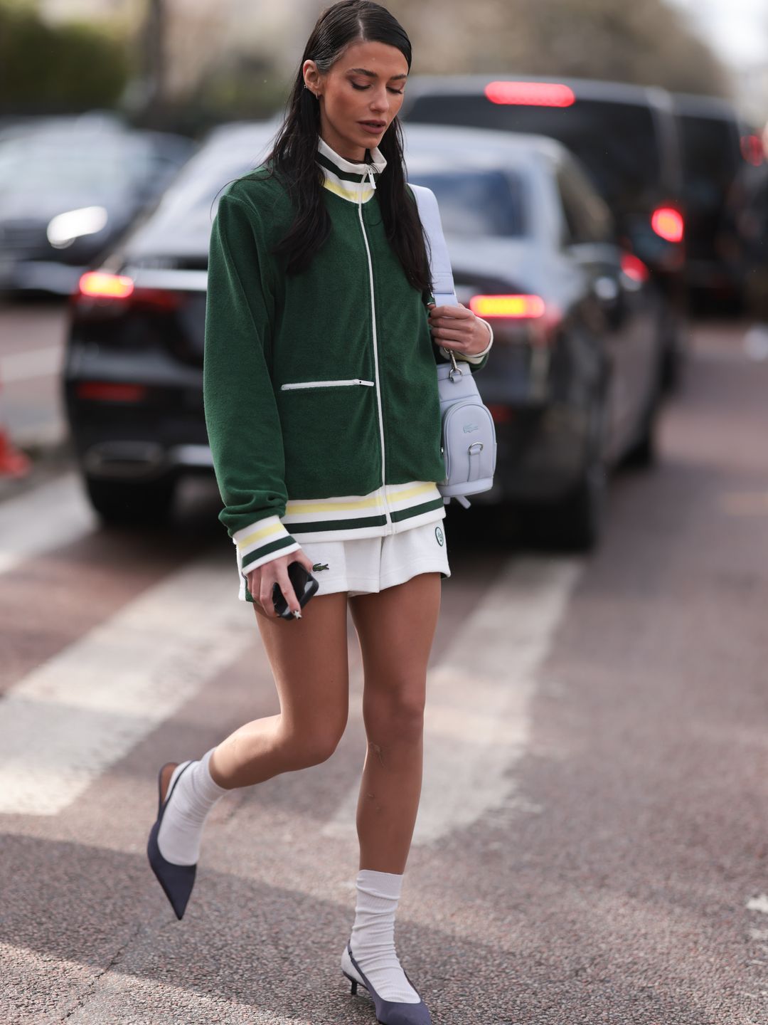Heloise Agostinelli seen wearing a green and white Lacoste tennis skirt, green Lacoste jacket, white socks, grey heels, Lacoste white leather bag outside Lacoste Show during the Womenswear Fall/Winter 2024/2025