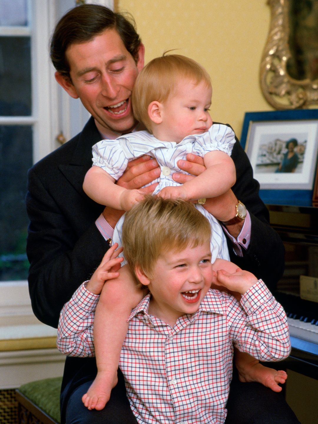 King Charles holding a baby Prince Harry on Prince William's shoulders