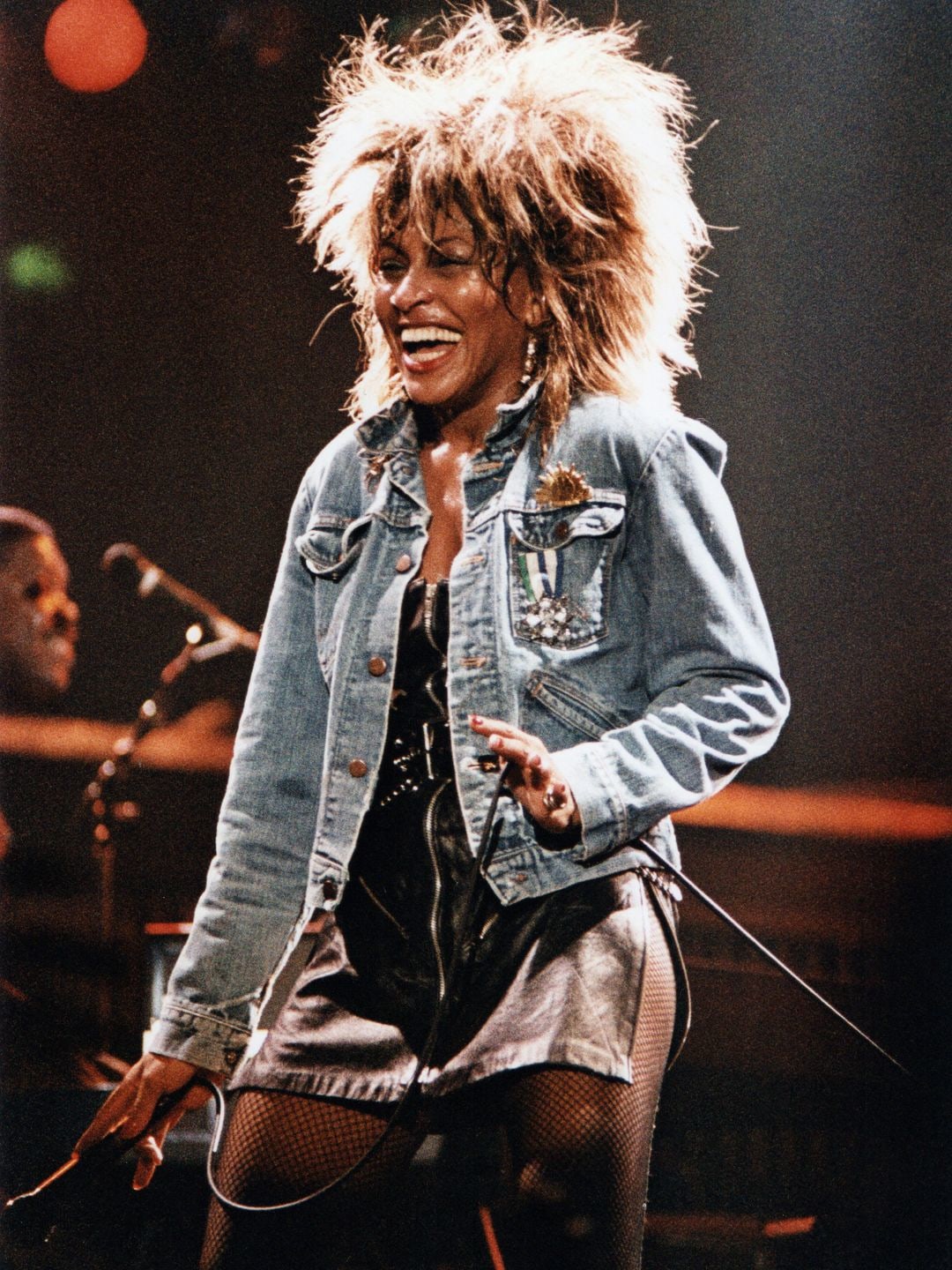 Tina Turner wearing a denim jacket and a leather zip-up mini dress