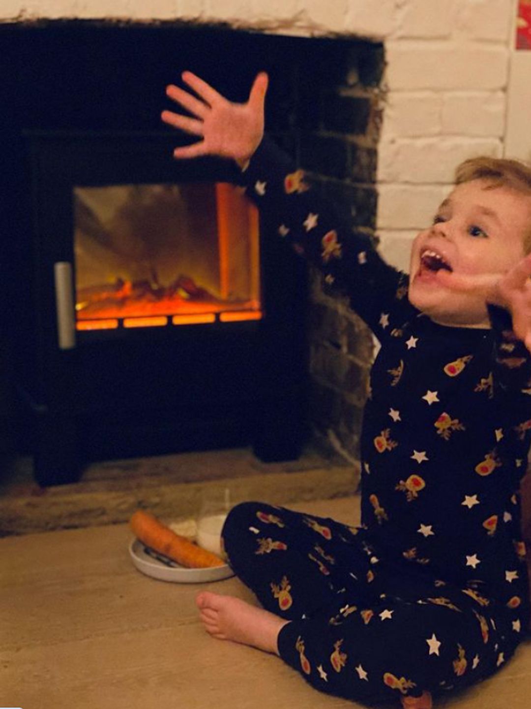 A young boy sitting by a fireplace