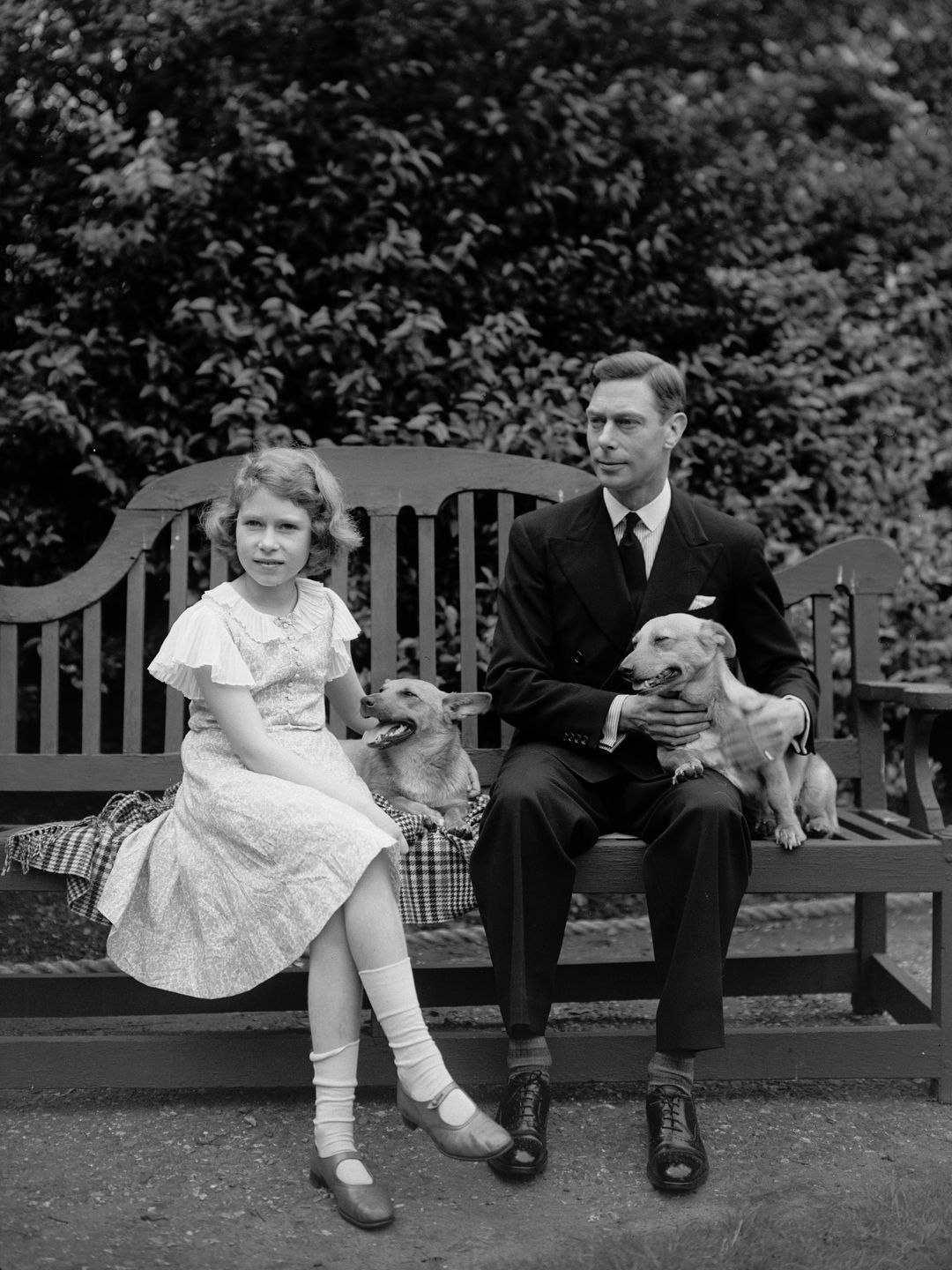 A young Queen Elizabeth sat with two corgis and King George VI
