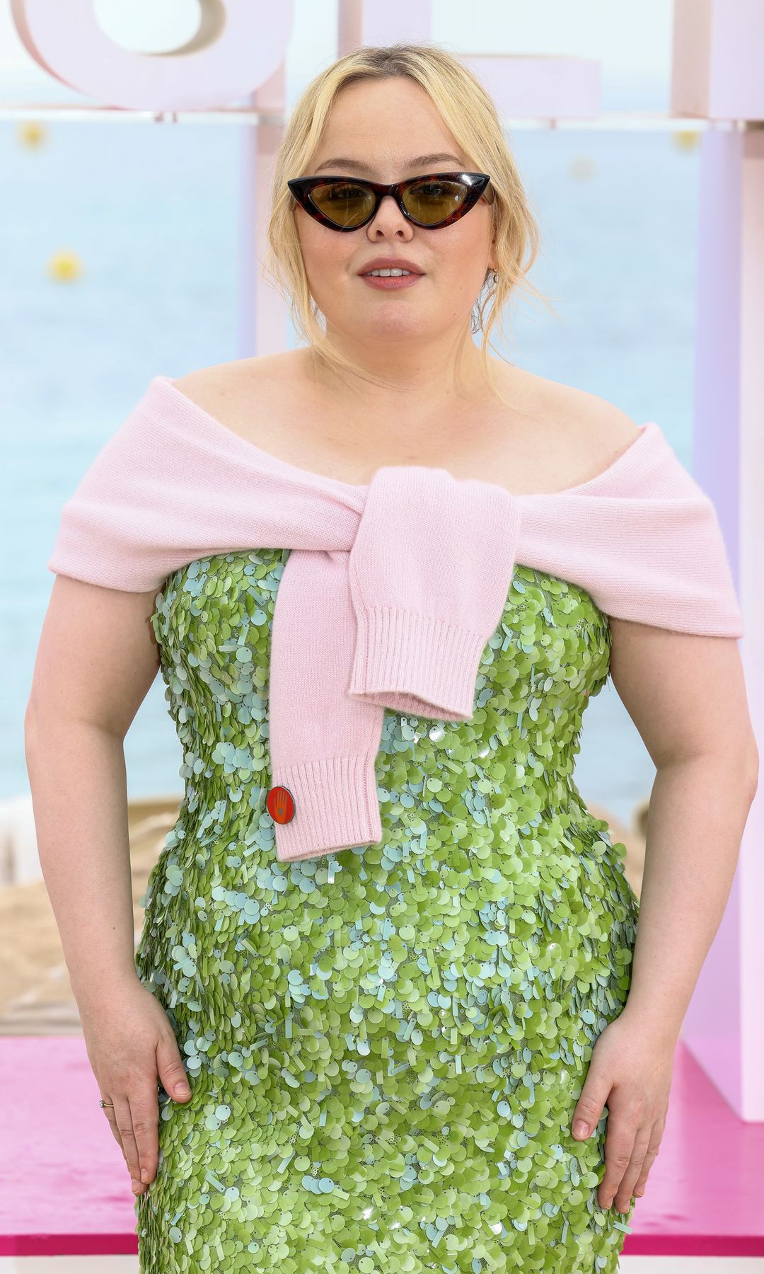 Nicola Coughlan attends the "Prix Konbini de l'Engagement" Photocall on Day Five during the 8th Canneseries International Festival at Palais des Festivals on April 28, 2025 in Cannes, France wearing a green sequin dress, sunglasses and a pink knit over her shoulders