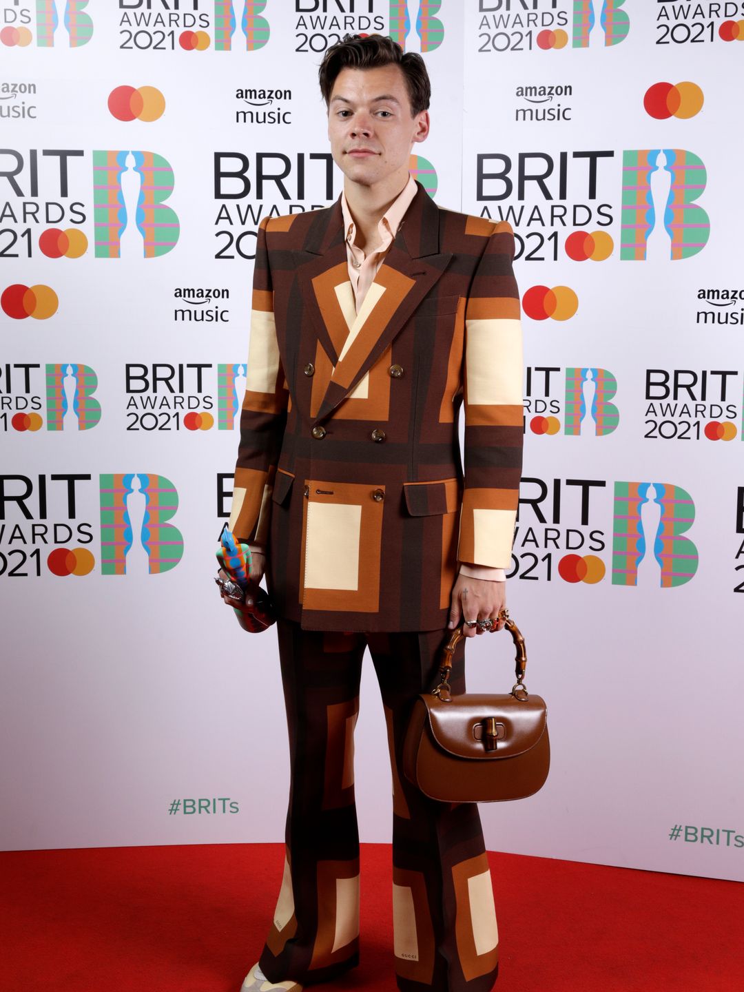 Harry Styles wins the Mastercard British Single award for Watermelon Sugar during The BRIT Awards 2021. He wears a brown Gucci suit with a brown leather handbag on the redcarpet