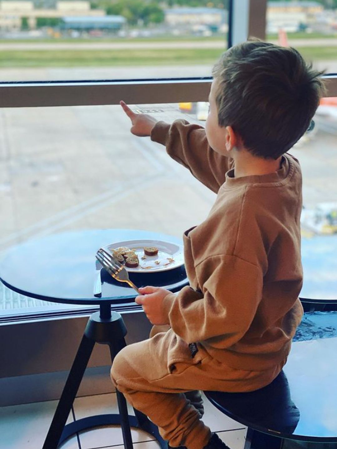 A young boy pointing at aeroplanes from inside an airport