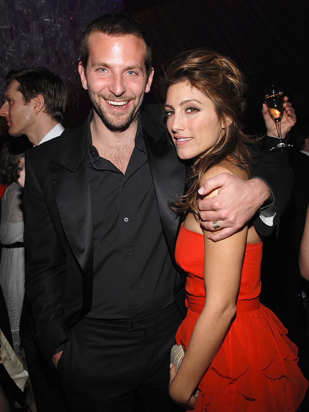 Jennifer Esposito wearing a red dress, cuddled up to Bradley Cooper in an all-black suit in 2007. 