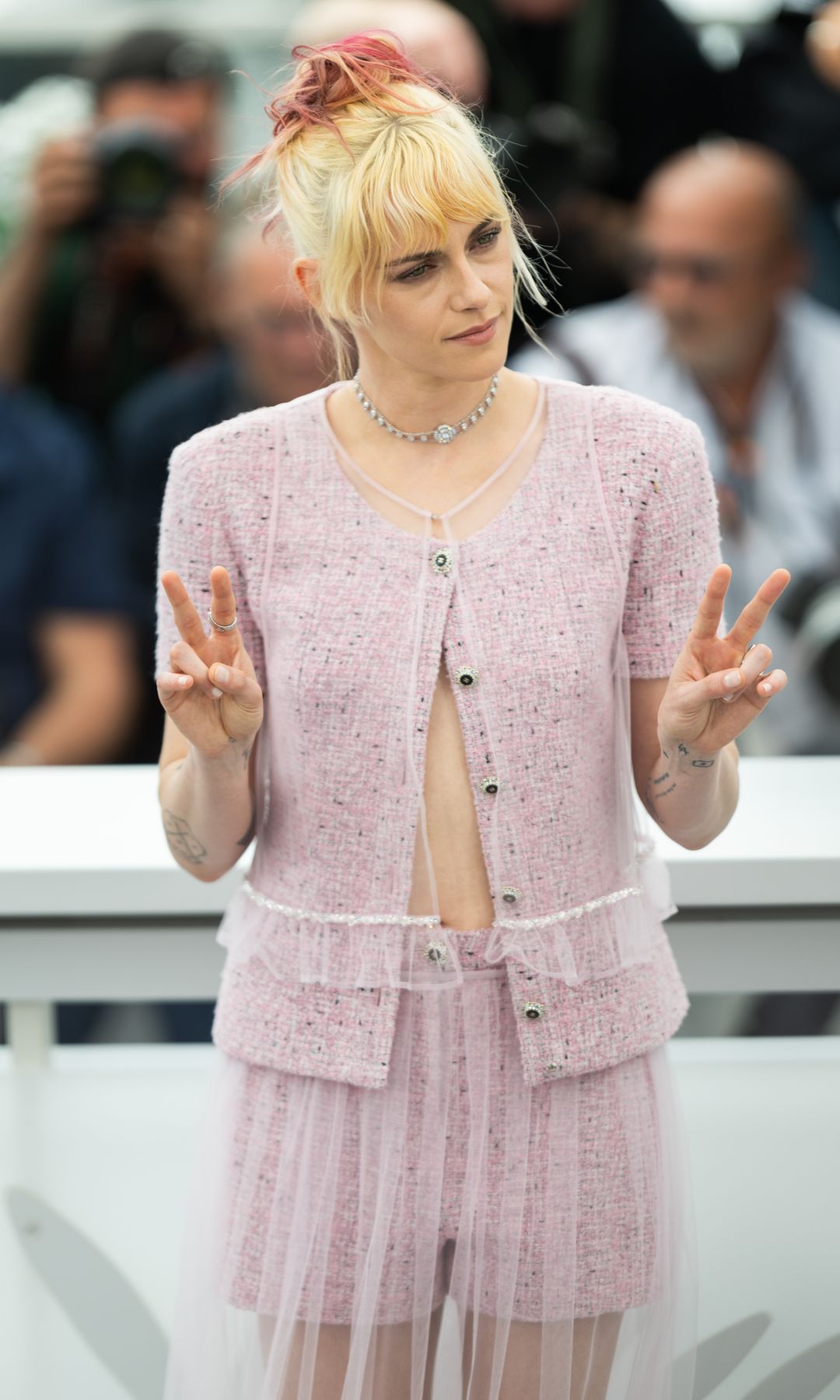 Kristen Stewart giving peace signs in a pink outfit
