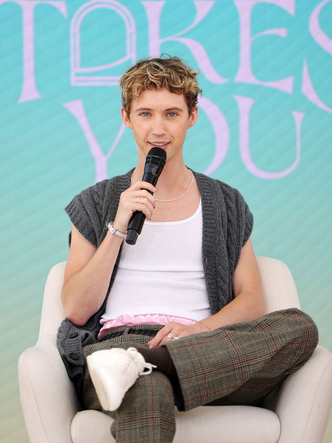 Troye Sivan holding a microphone in woollen jacket and white top