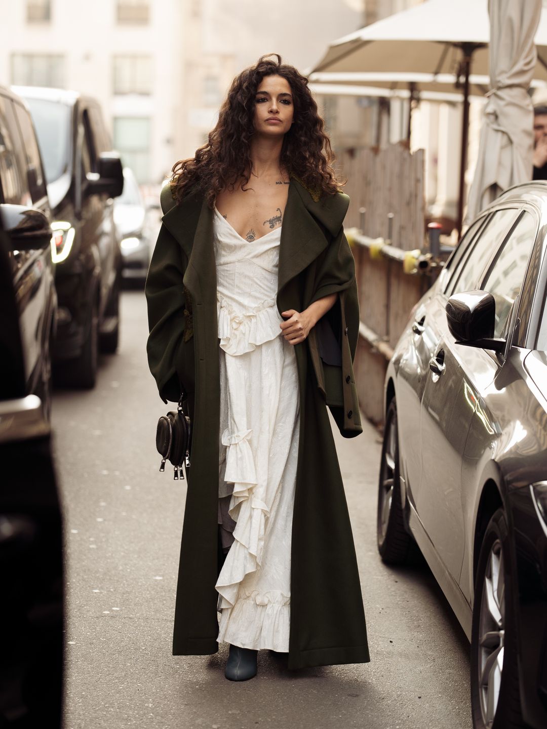 Chiara Scelsi wears a long white maxi dress and dark green coat outside Del Core 