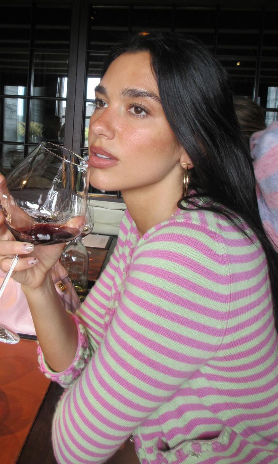 Dua Lipa shares a snap of her sipping on red wine in a pink and green striped Chanel outfit