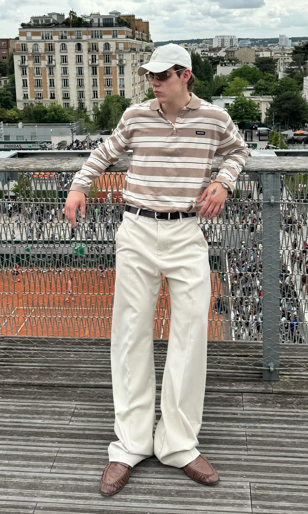 The Kid Laroi poses in cream trousers and a stripe shirt at The French Open