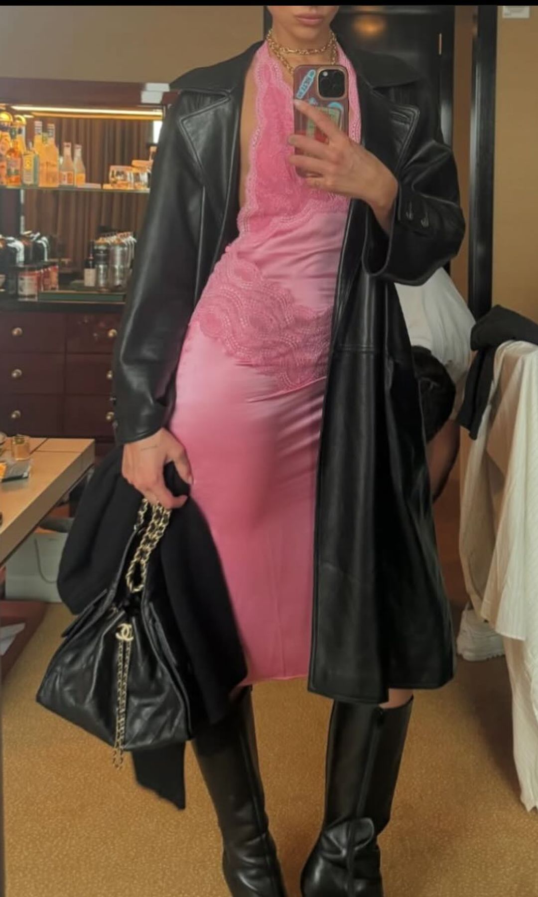 Dua Lipa poses for a mirror selfie in a pink slip dress, black boots and a black coat