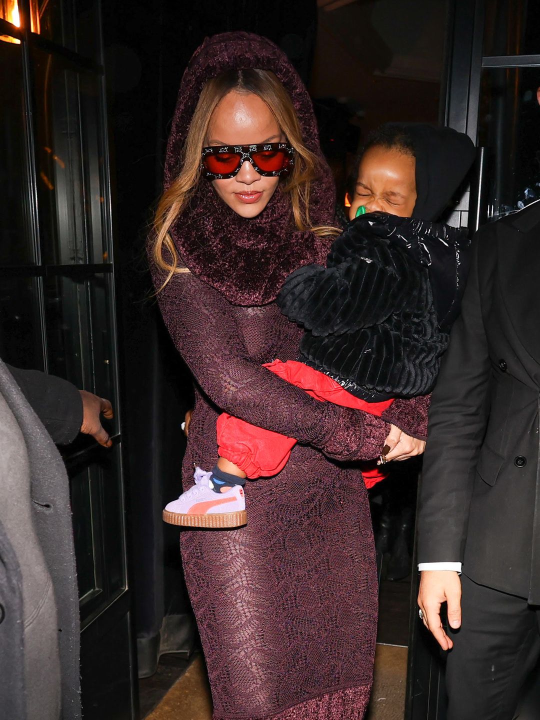 Rihanna carries her son RZA in a red wine hued dress and pair of gucci sunglasses while in Paris