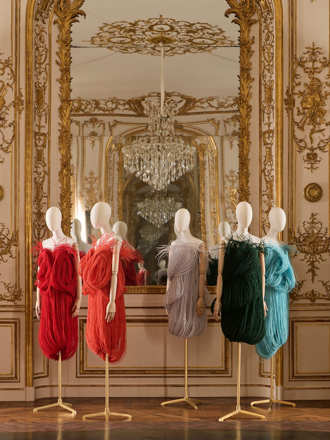The Loewe AW25 Collection is displayed in a grand gilded room. Five mini dresses in bright colours are displayed on mannequins.