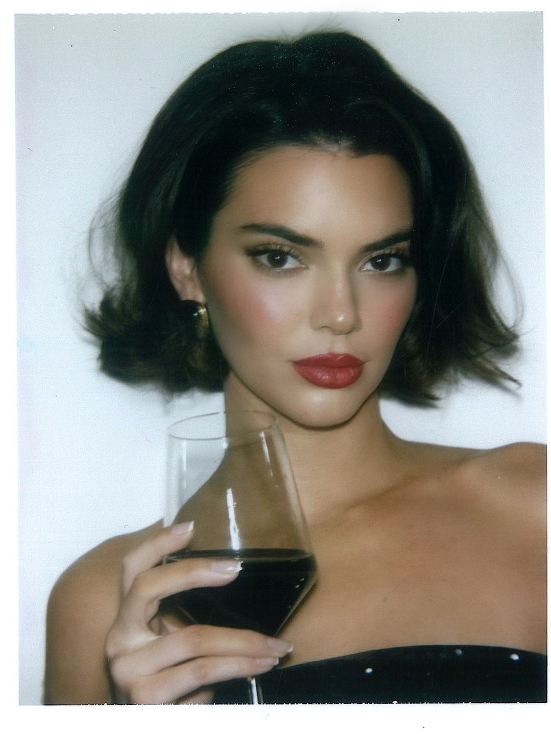 Kendall Jenner poses for a photo wearing a pair chunky earrings and a glass of red wine 