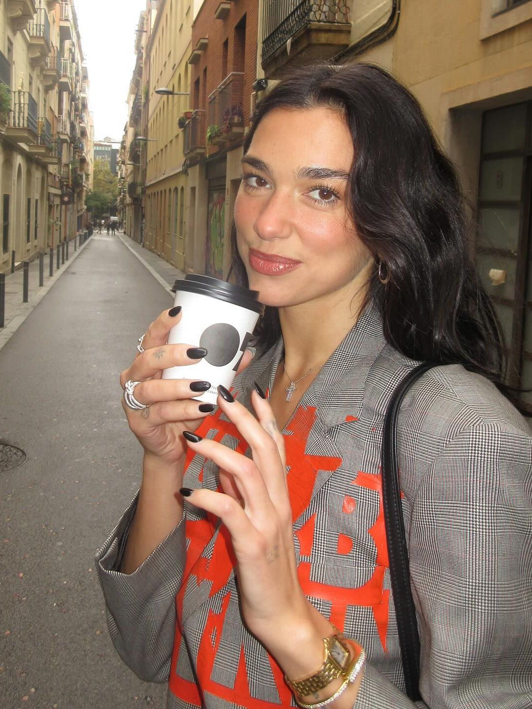 Dua Lipa poses for a photo while drinking a coffee wearing a printed blazer 