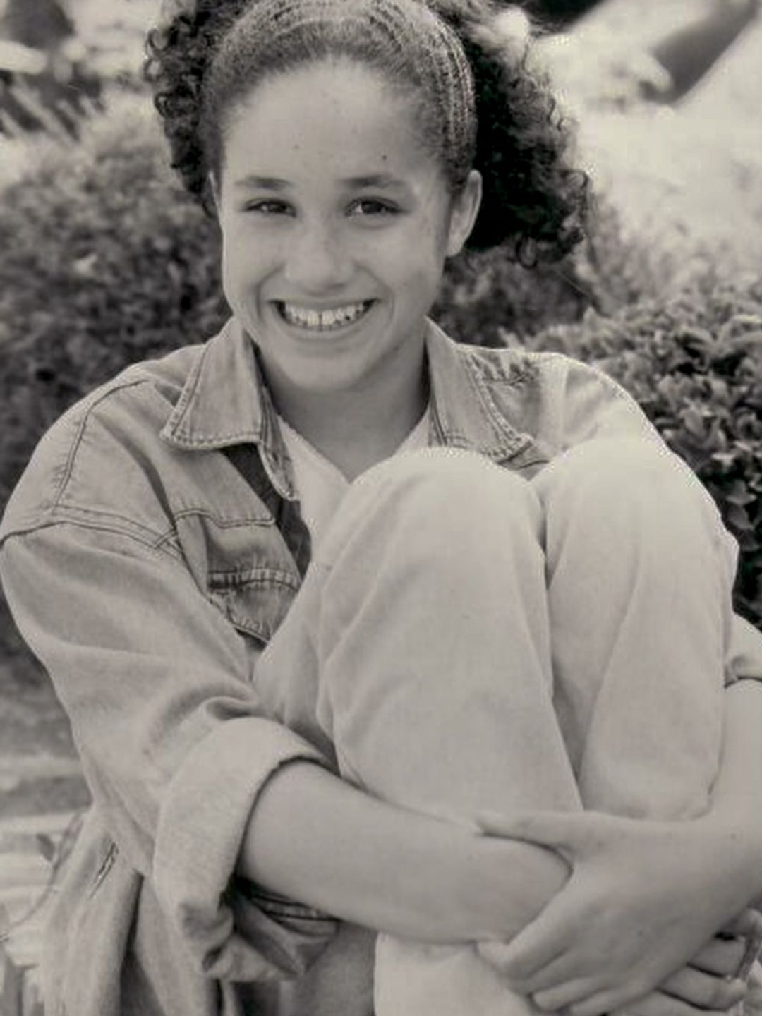 A black-and-white photo of a young Meghan Markle in a denim jacket and jeans