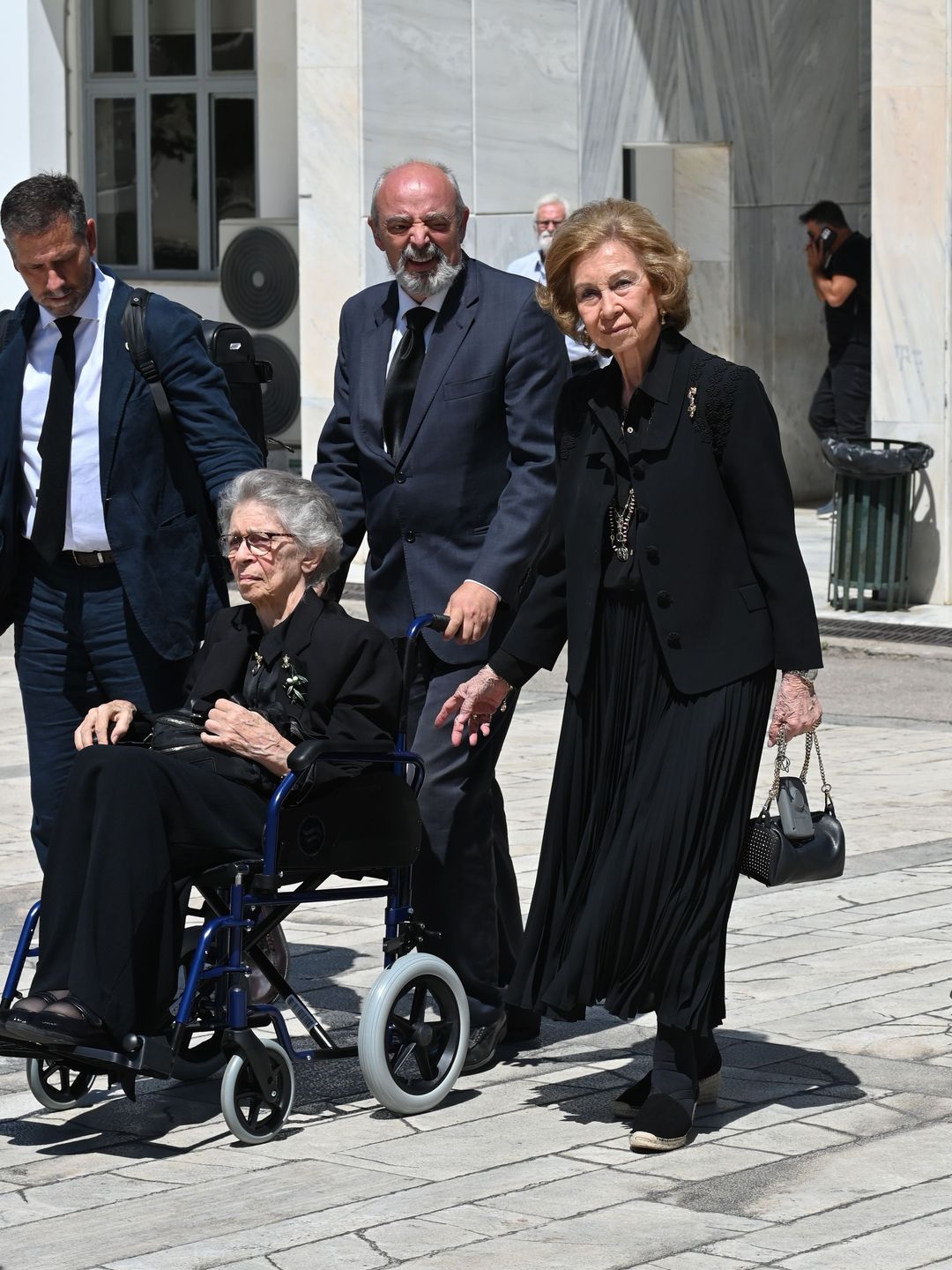 Princess Irene being pushed in a wheelchair as Queen Sofia walks next to her